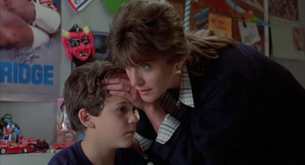 An 80s mother and son. The mother checks the boy's temperature with her hand.